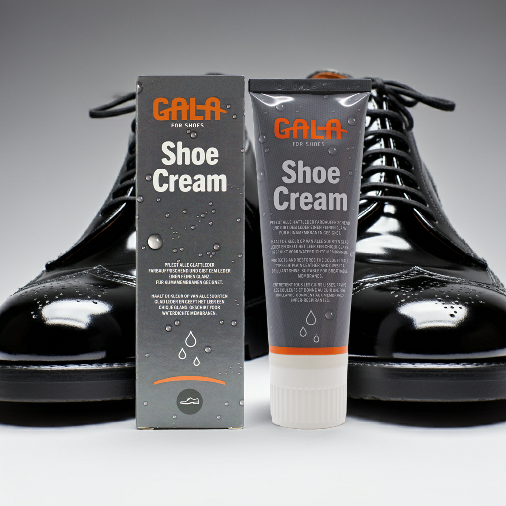CasaBellissimo GALA Lackpflege in der Tube mit Umverpackung auf weißem Untergrund und im Hintergrund ein paar hochglänzende schwarze Lackschnürschuhe