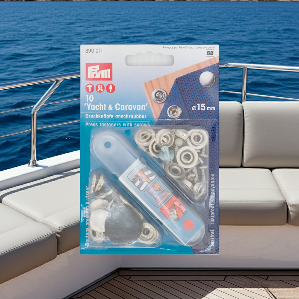 Prym Druckknöpfe "Yacht & Caravan", nähfrei, anschraubbar, Ø 15 mm silberfarbig und mit Werkzeug in der Blister Verpackung im Hintergrund das Meer und eine cremefarbene Ledereckcouch auf einer Yacht mit silberner Reling