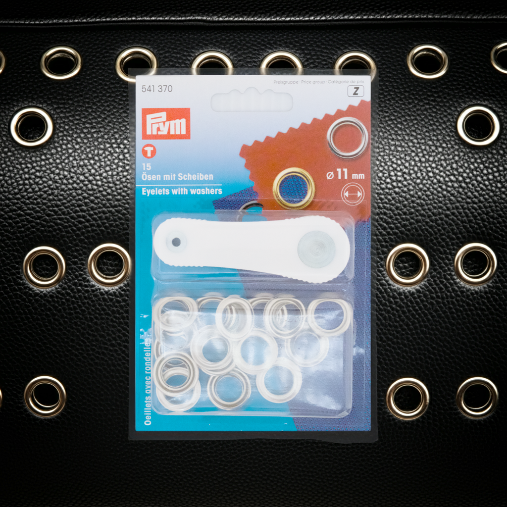 Prym Ösen mit Scheiben, Ø 11 mm silberfarbig und mit Werkzeug in durchsichtiger Verpackung auf schwarzem Lederhintergrund mit mittleren Ösen