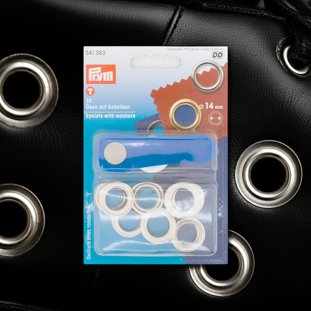 Prym Ösen mit Scheiben, Ø 14 mm silberfarbig und mit Werkzeug in durchsichtiger Verpackung auf schwarzem Lederhintergrund mit großen Ösen